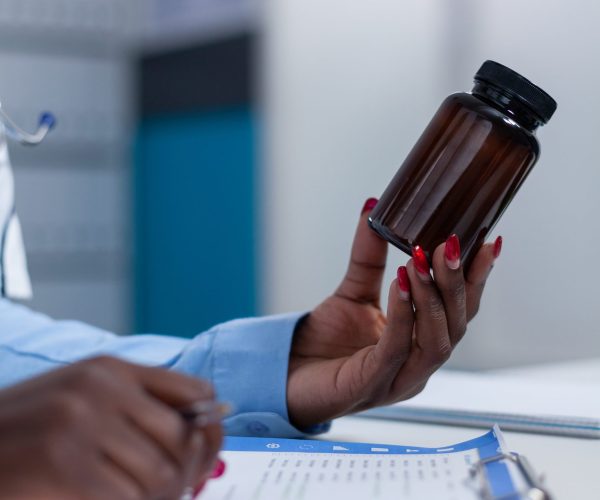 Close up of hospital general practitioner specialist holding a vial of medicine while checking symptom list and patient illness history. Medic having antiviral bottle in hand
